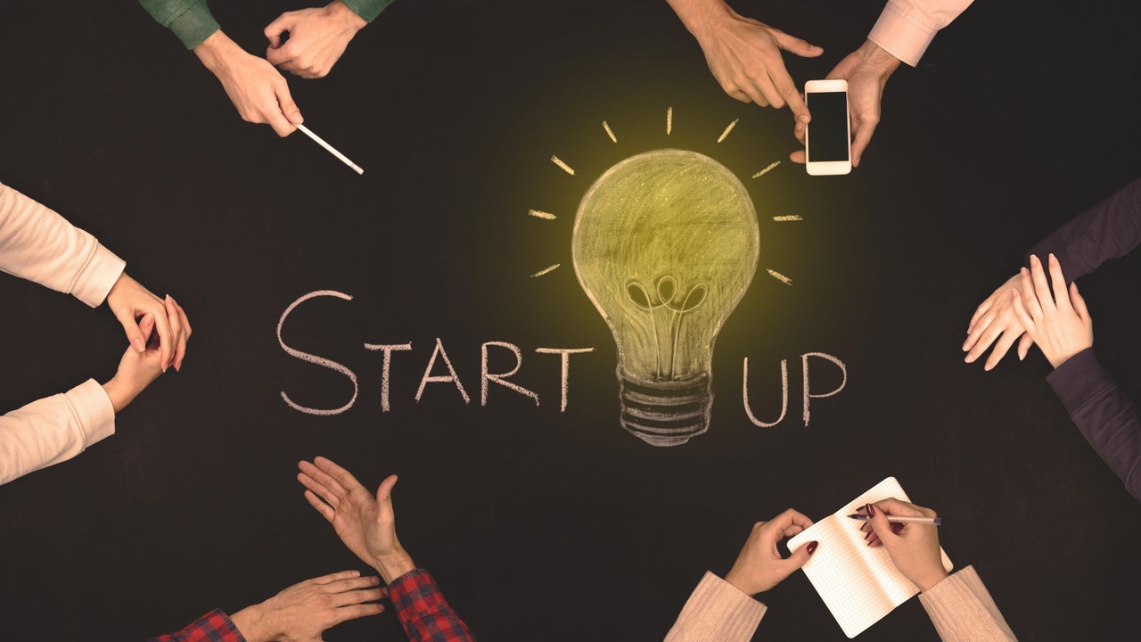 People sitting around a table--the word "Startup" is in the middle of the table, with a lit lightbulb in the middle of the word